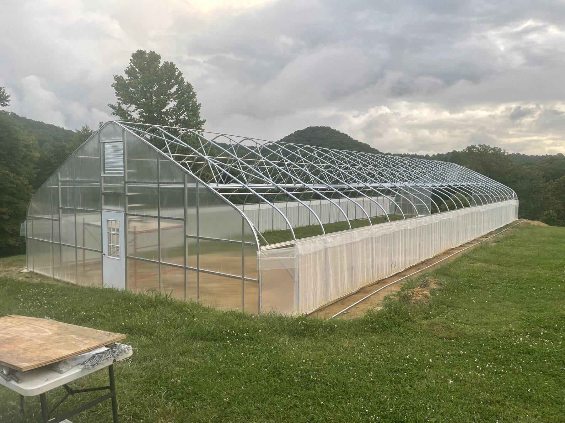 The farm's high tunnel greenhouse on a grassy rise with mountains behind