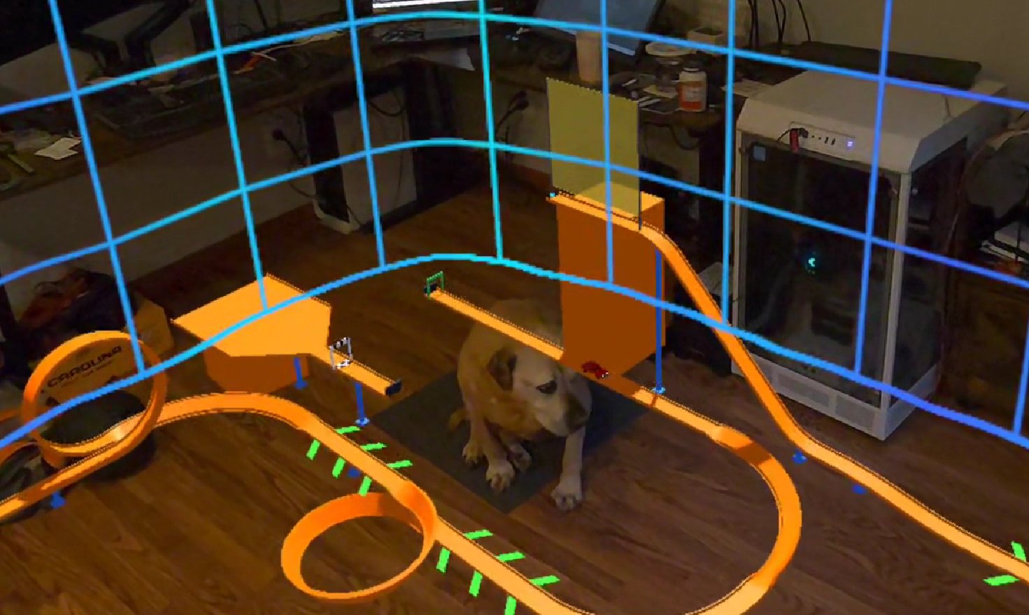 Mixed-reality view of orange toy-car track with loops and ramps built around a real room, with a dog sitting in the middle of the course